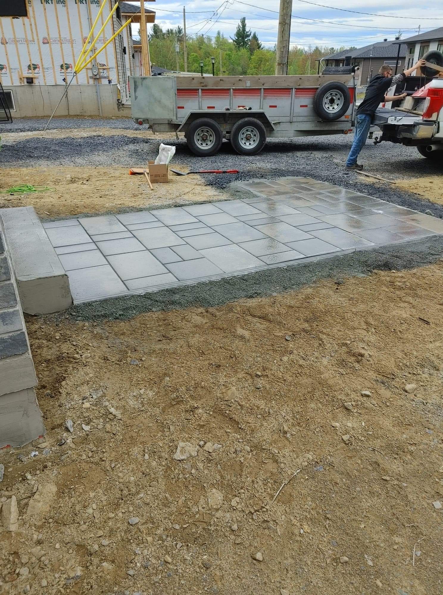 Chantier : Pose de pavés pour une terrasse. Un homme travaille près d’une remorque, un camion étant visible en arrière-plan.