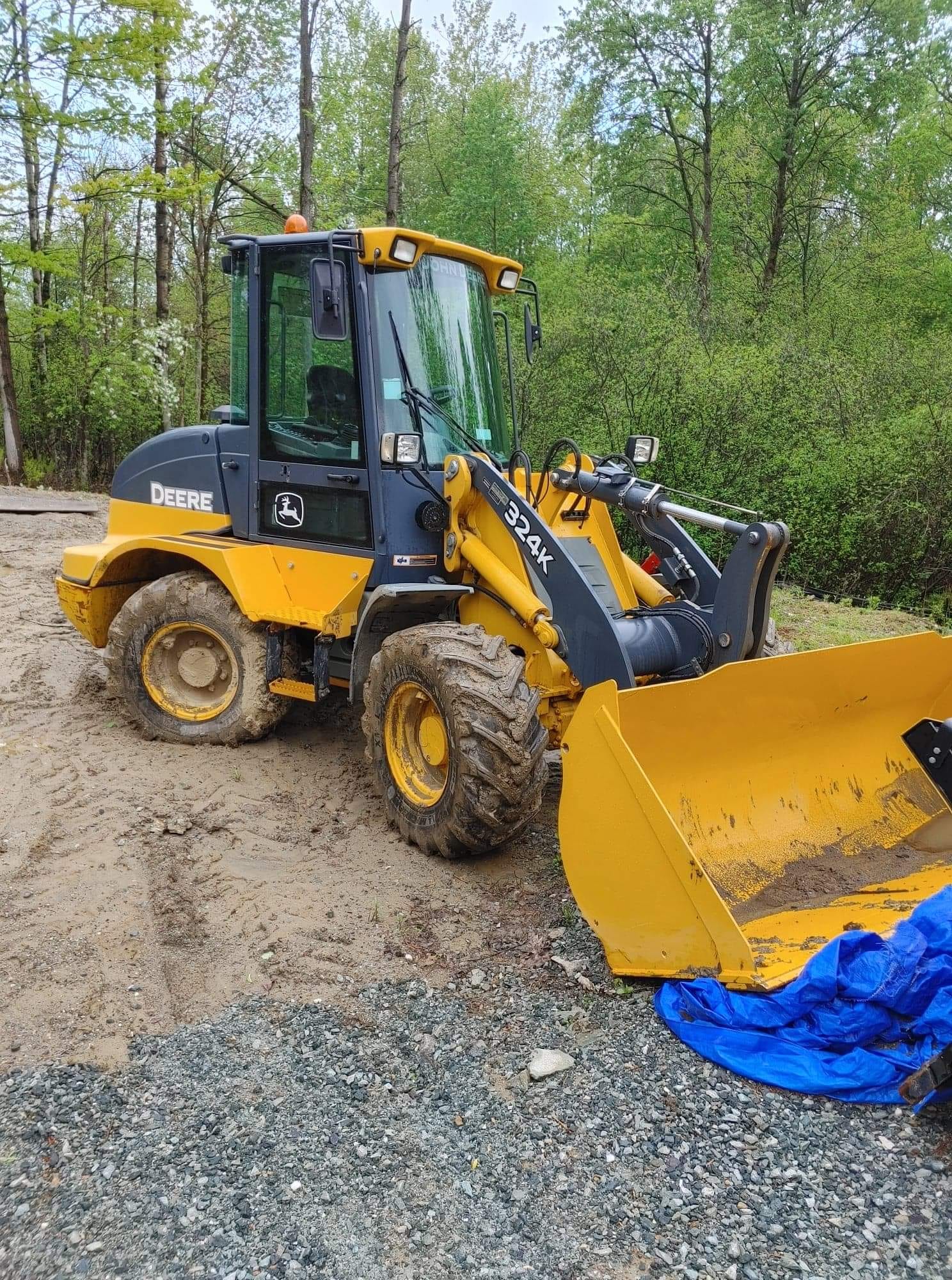 Chargeuse sur pneus John Deere 324K jaune et noire sur une surface de terre avec une bâche bleue.