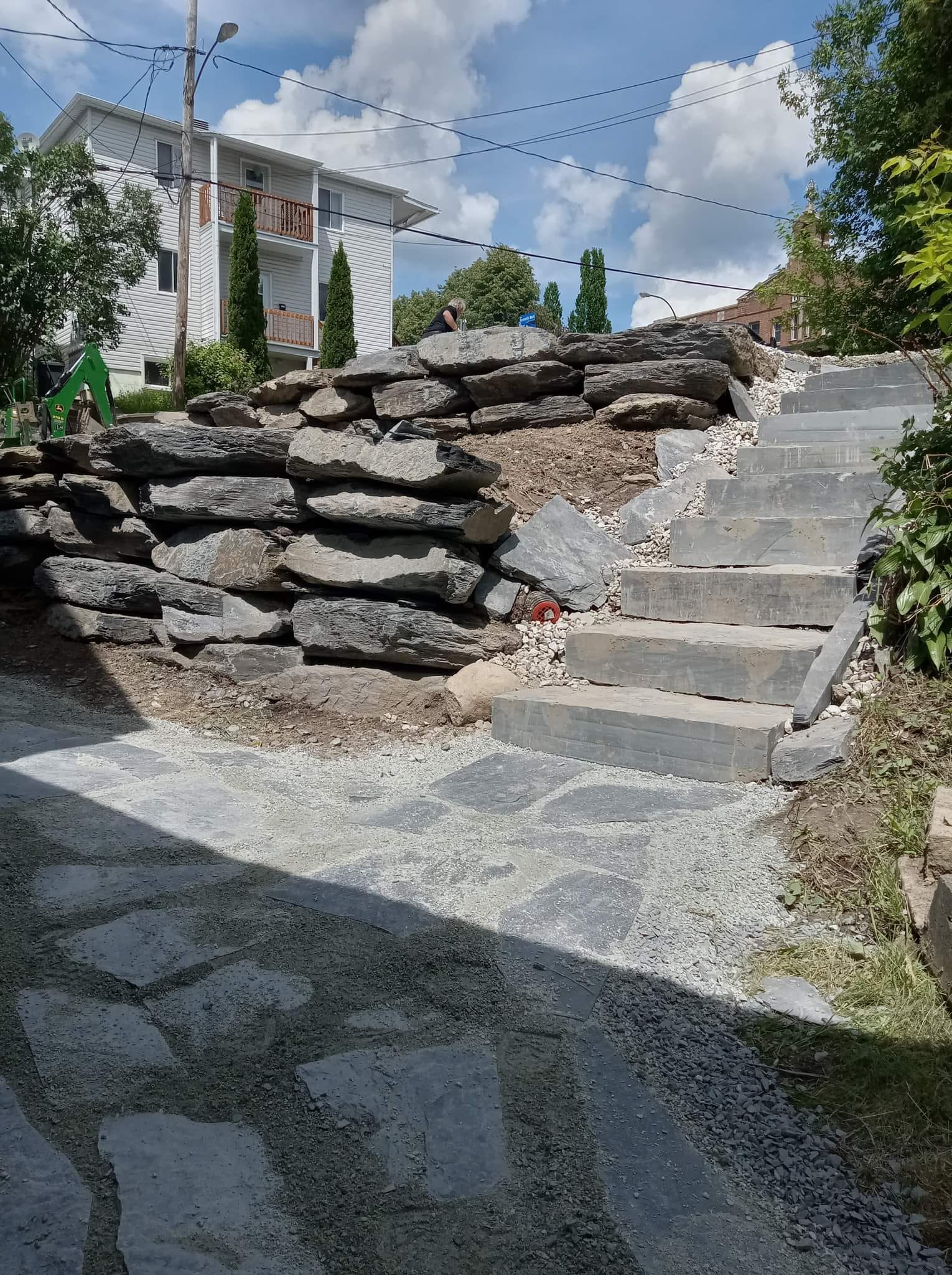 Des marches et un chemin de pierre longent un mur de soutènement en pierres empilées. 