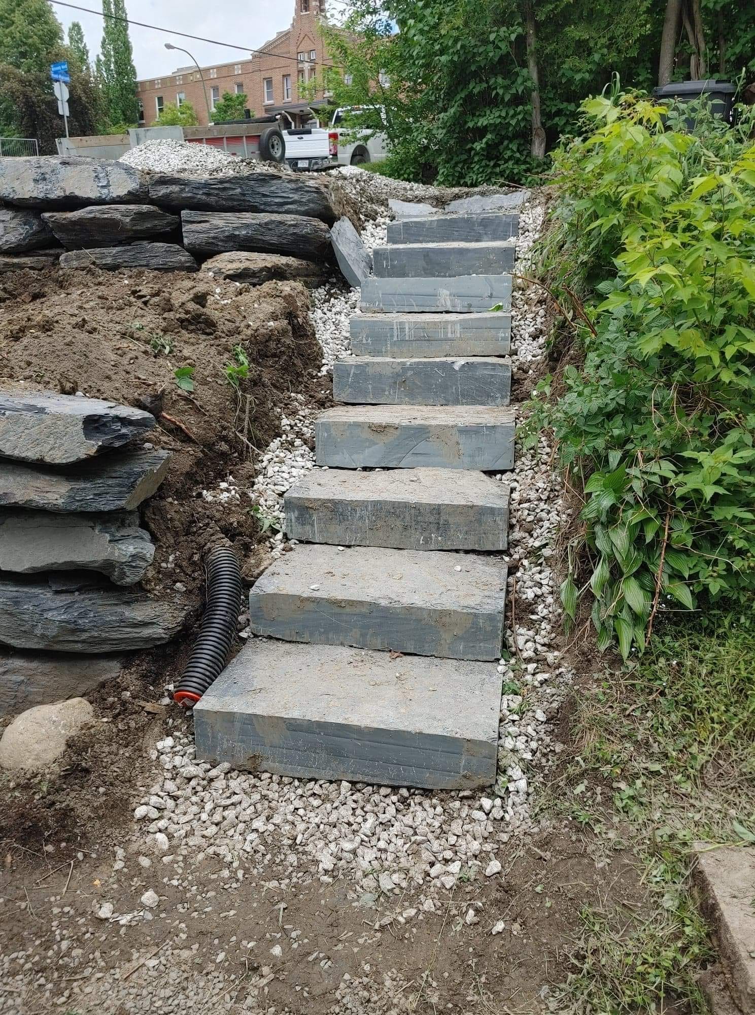 Des marches en pierre montent à flanc de colline, bordées de terre et de gravier, avec une église visible en arrière-plan.