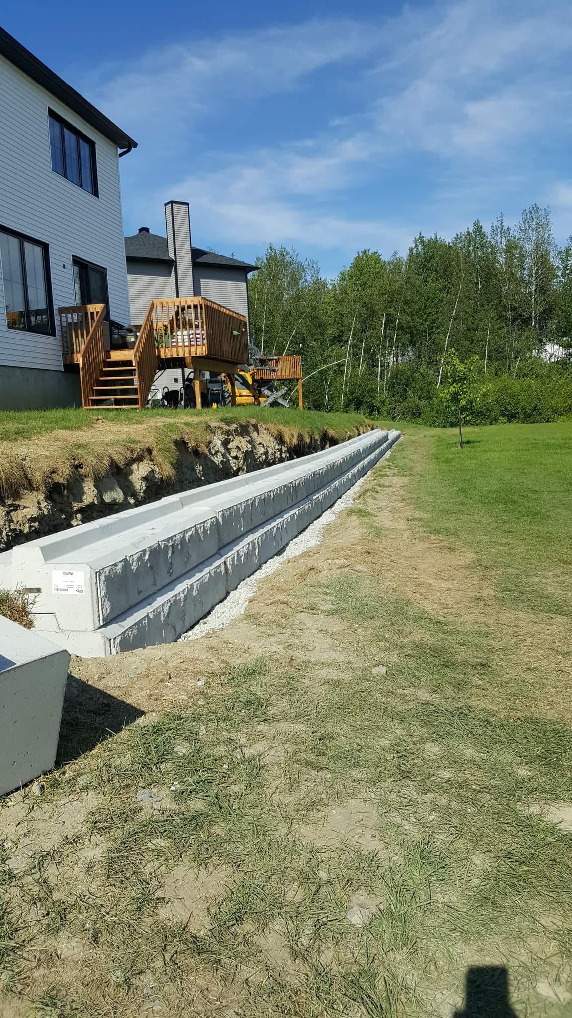 Mur de soutènement en béton en construction dans une cour, avec une terrasse en arrière-plan, par une journée ensoleillée.