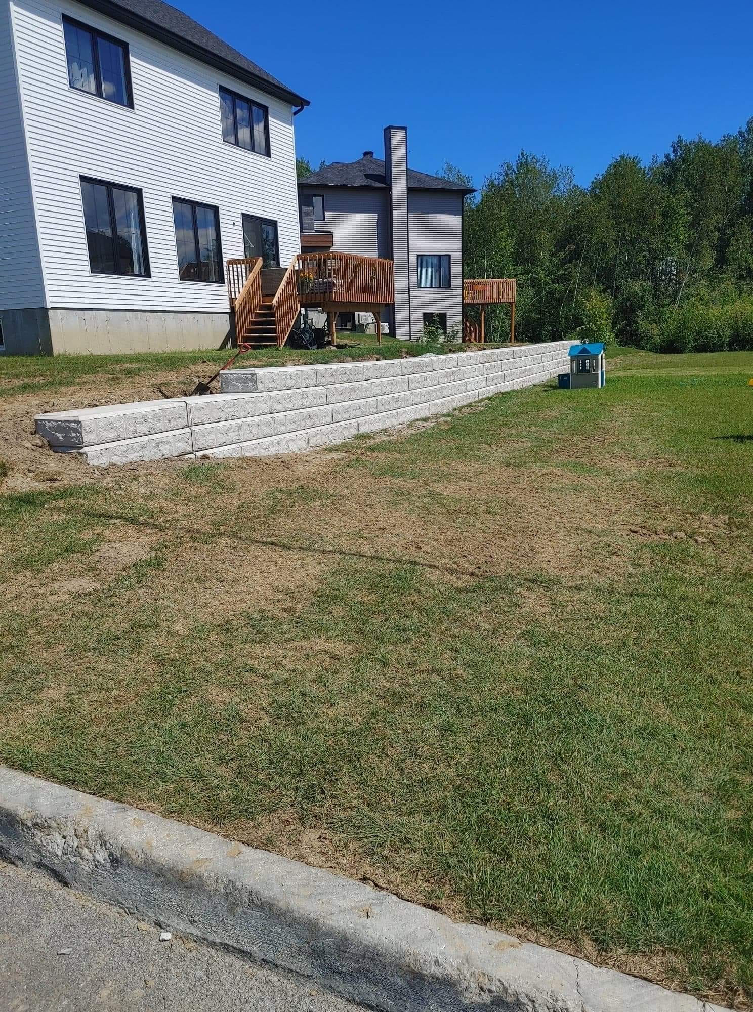 Par une journée ensoleillée, un mur de soutènement en blocs gris descend en pente douce le long d'une pelouse.