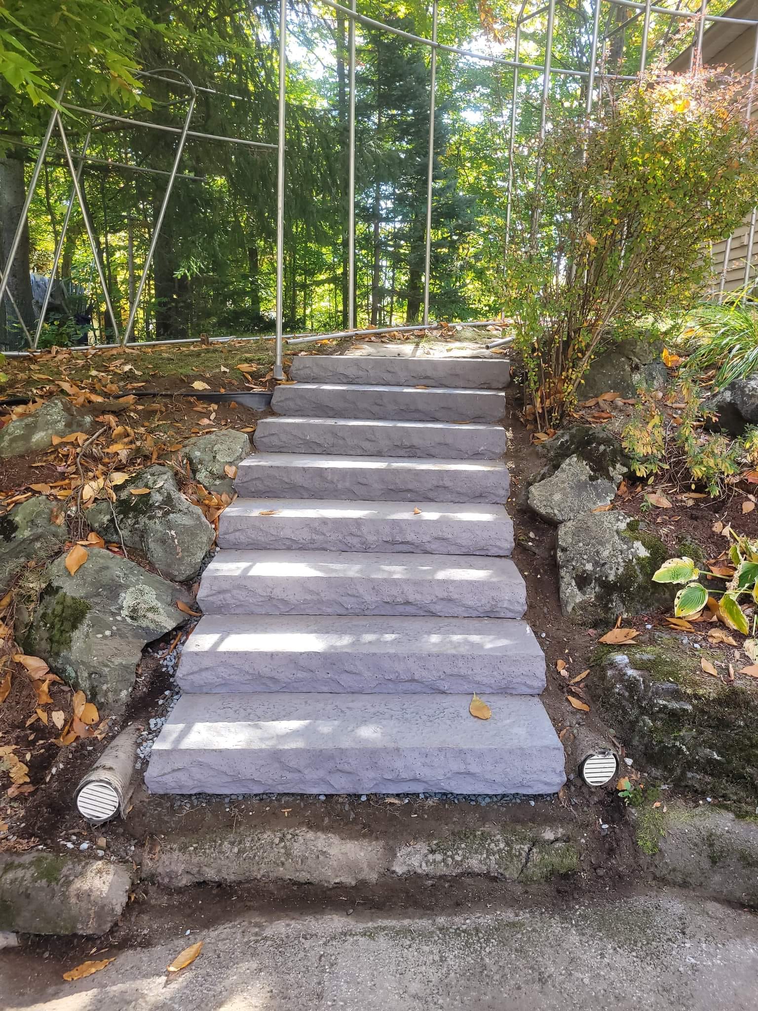 Des marches en pierre mènent à flanc de colline, bordées de rochers et de végétation, avec une rambarde métallique.