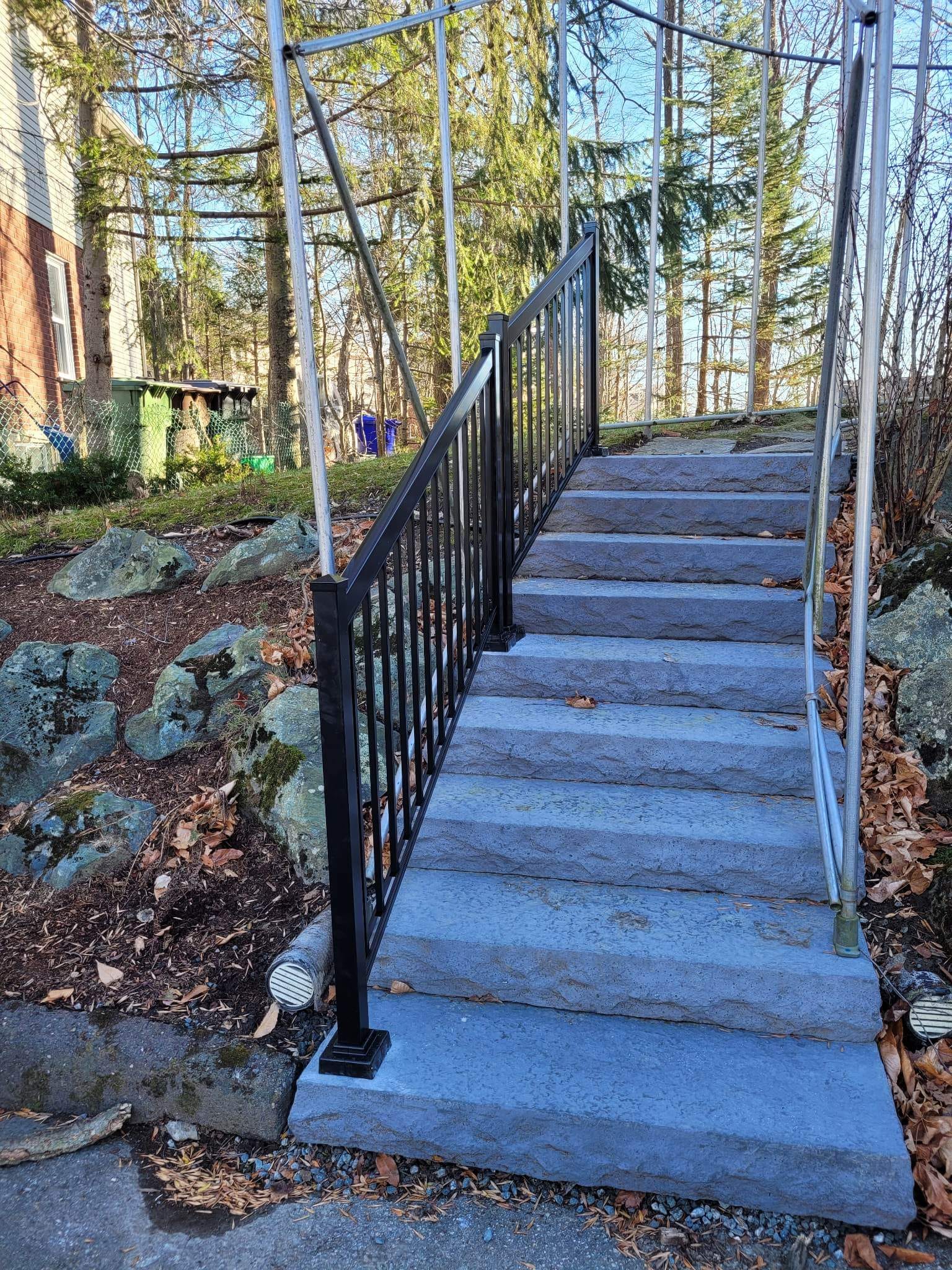 Escalier en pierre avec rambarde noire menant à l'étage, en extérieur.