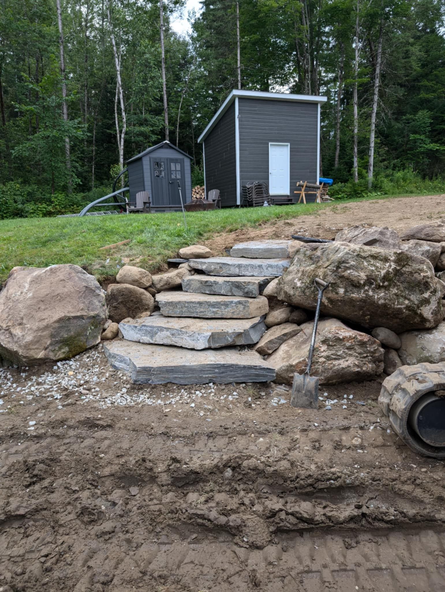 Des marches en pierre mènent à deux petits bâtiments gris situés dans une zone boisée.