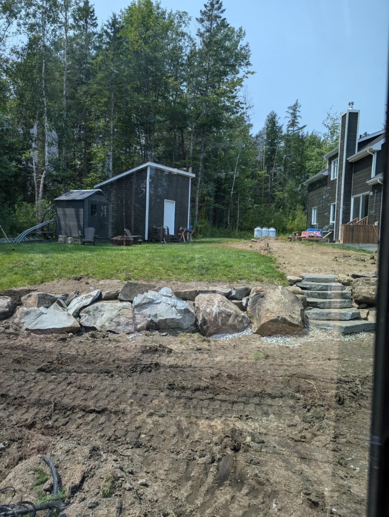 Une scène de jardin avec aménagement paysager : un mur de soutènement en pierre, des marches, un petit abri de jardin.