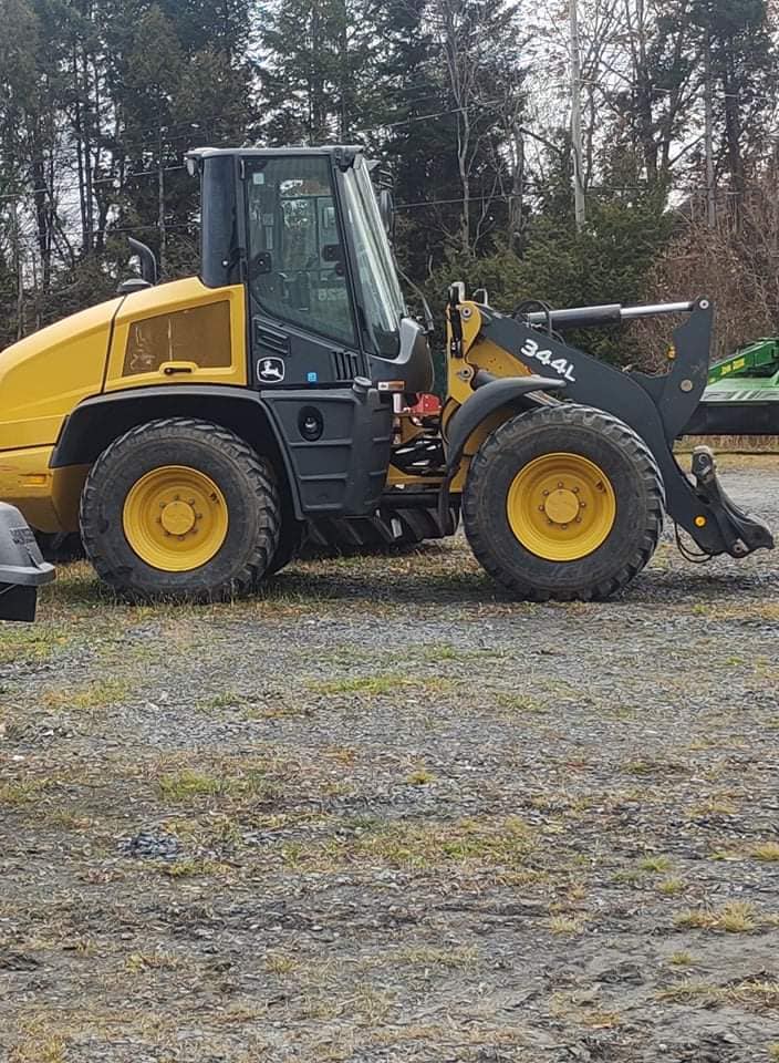 Chargeuse sur pneus John Deere jaune et grise sur du gravier, en extérieur.