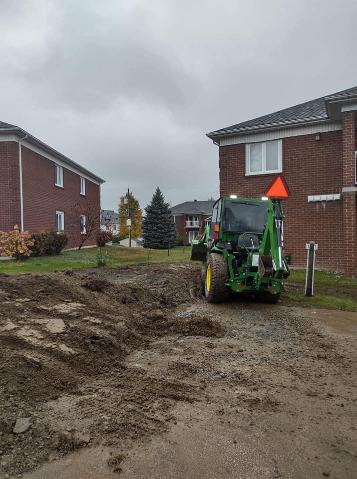 Un tracteur vert se trouve sur un terrain boueux entre deux bâtiments en briques.