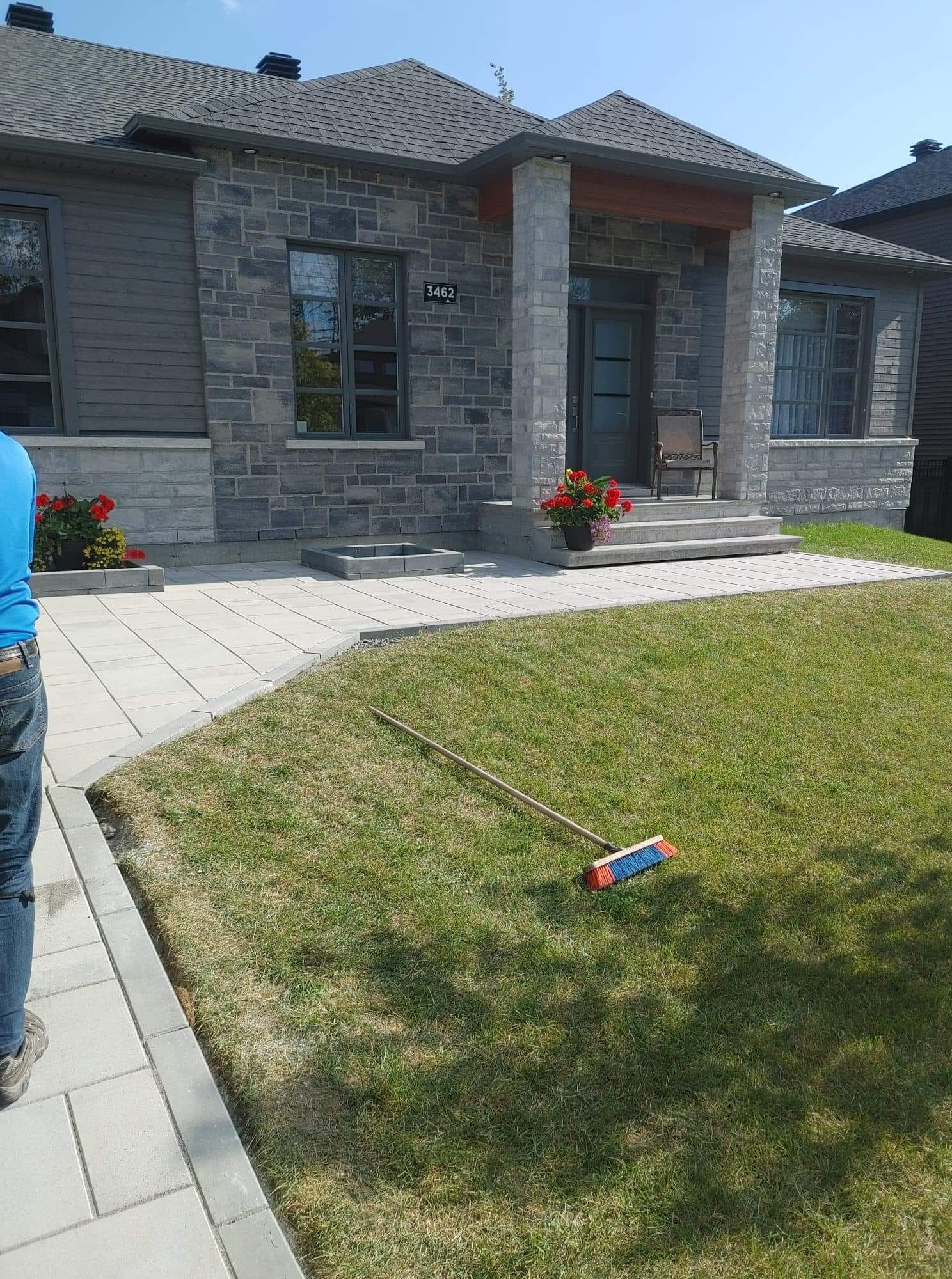 Une maison en pierre avec un balai à manche bleu sur la pelouse devant.