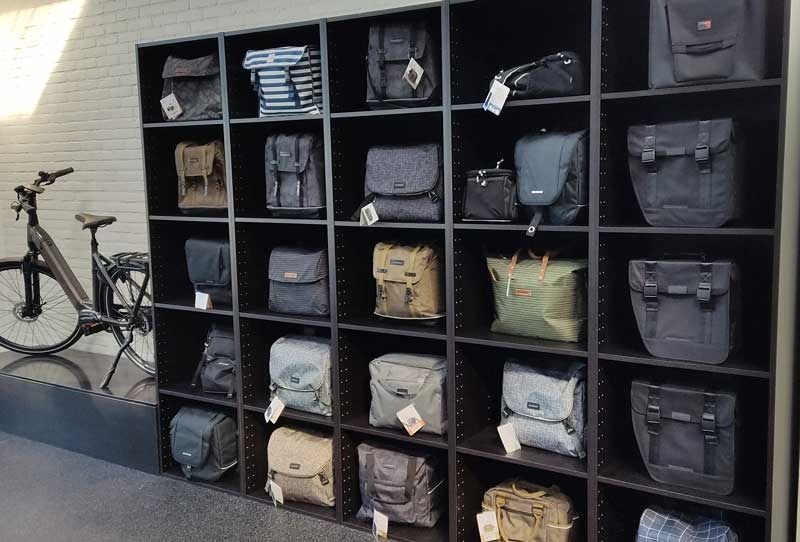 Twee mannen op e-bikes voor een fietsenwinkel met een logo.