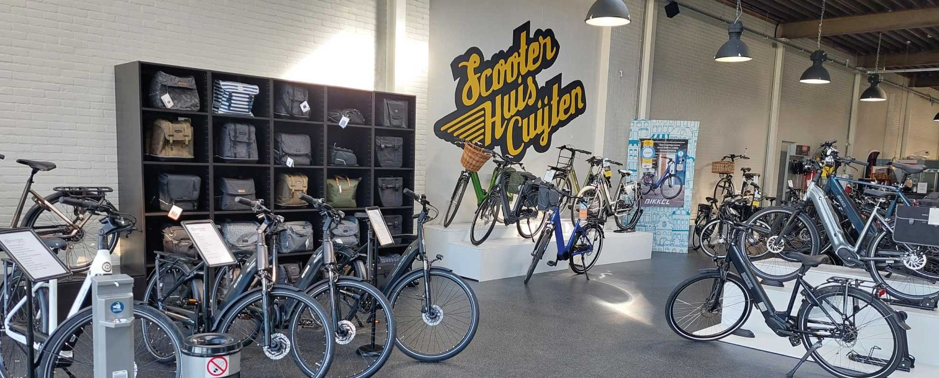 Fietsen uitgestald in een winkel met schappen vol tassen. Op een bordje staat 