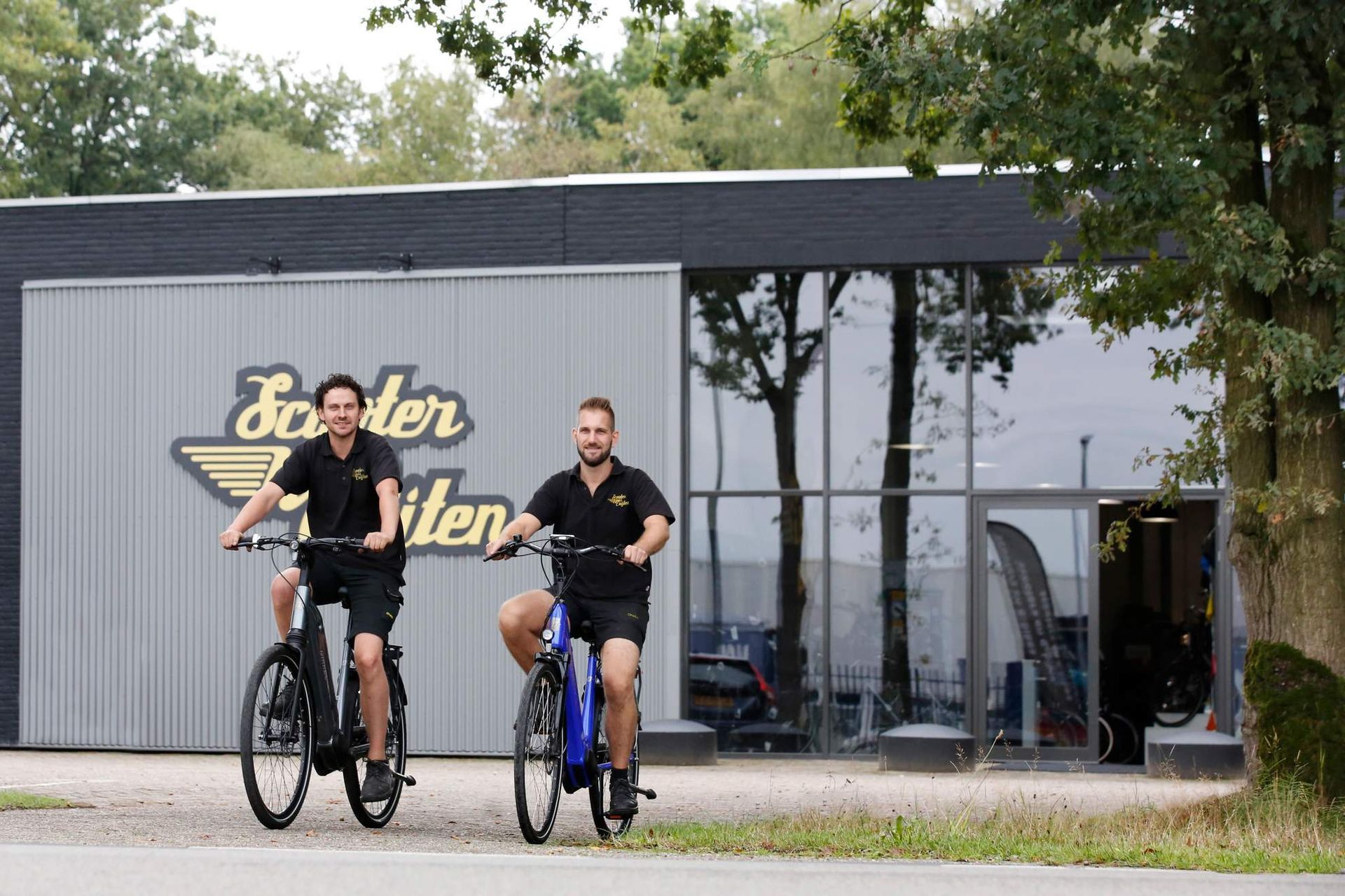 Twee mannen op fietsen voor een fietsenwinkel, het bord 