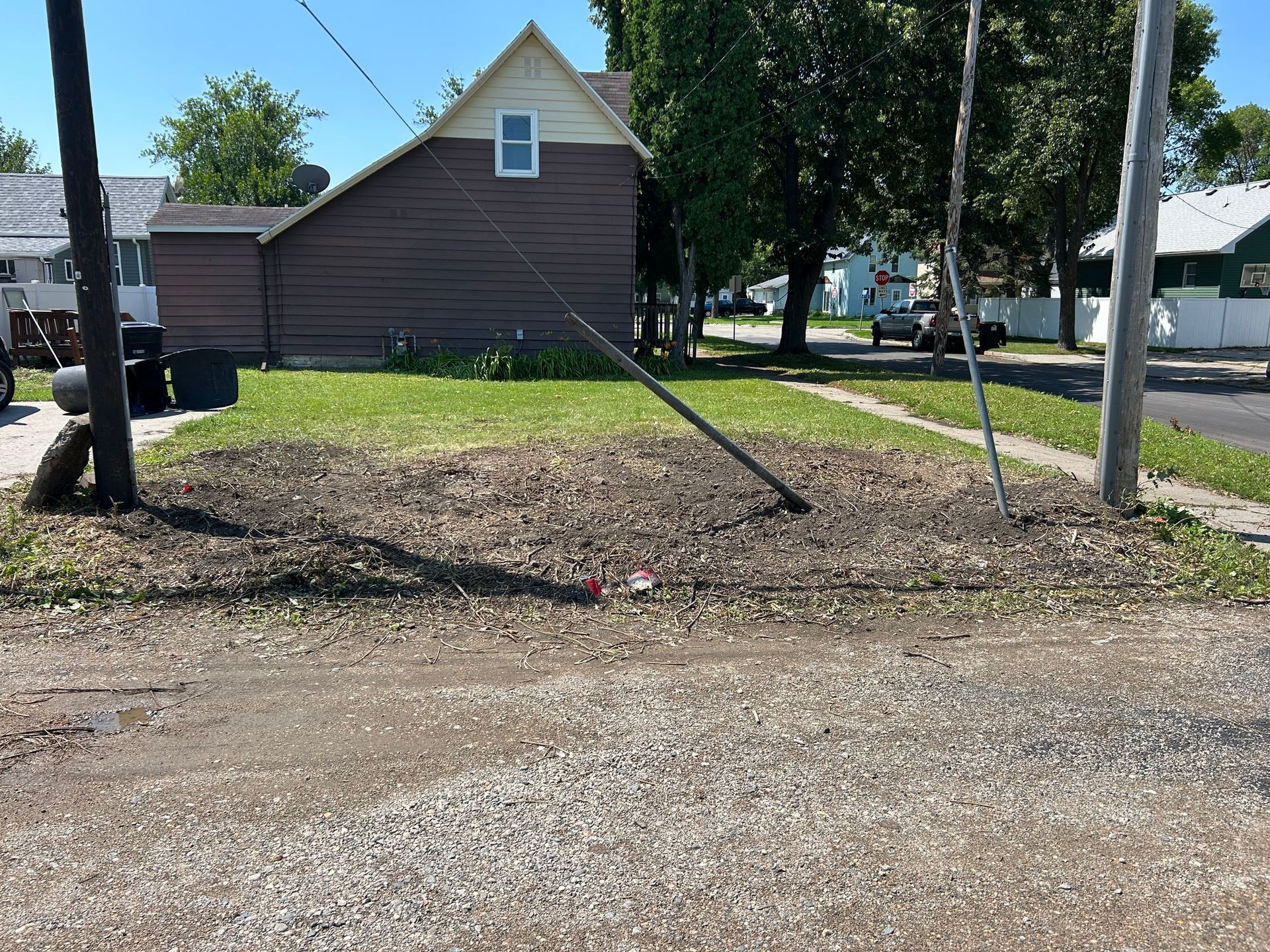 House with slanted utility poles beside a gravel lot and trees in a residential area