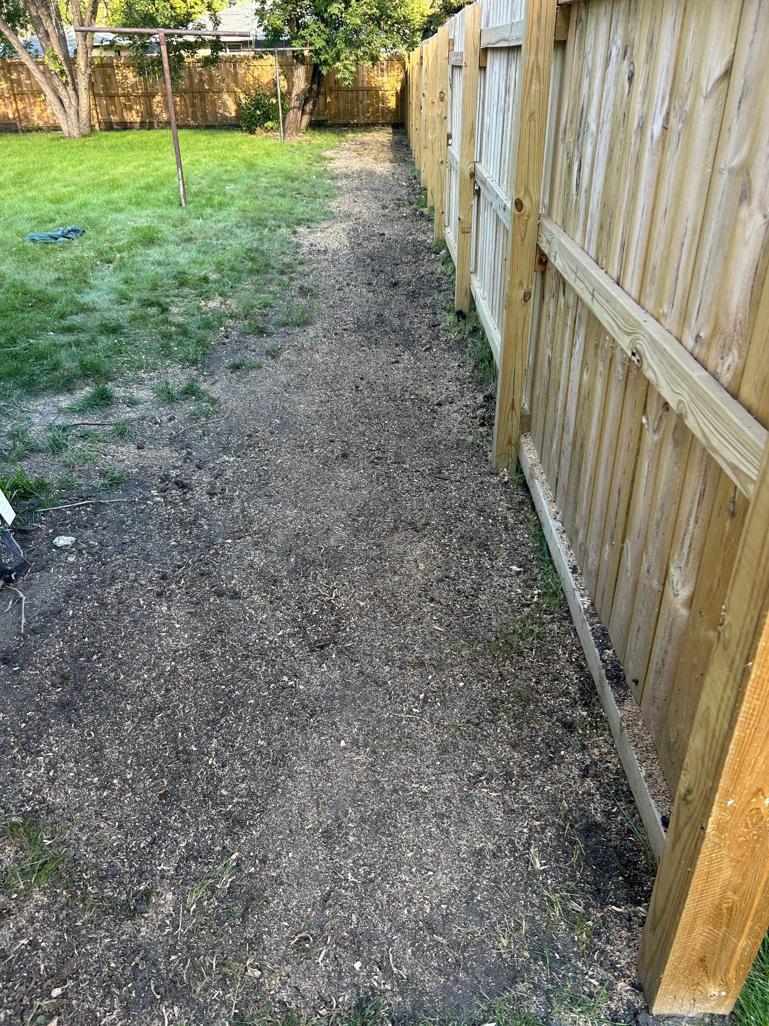 Gravel path beside a wooden fence leading to a grassy yard in sunlight