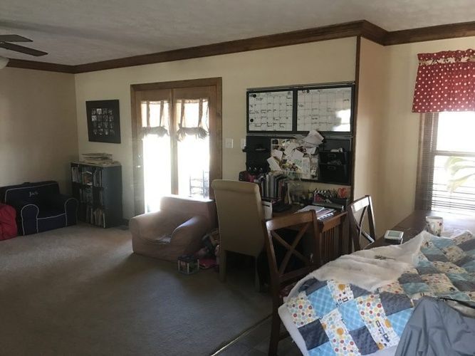 A living room with a bed , chair , desk and sliding glass doors.