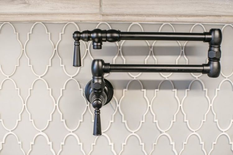 Two black faucets are hanging on a tiled wall.