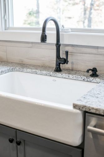 A white farmhouse sink with a black faucet in a kitchen.