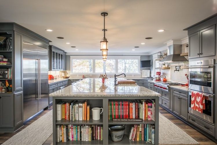 A kitchen with gray cabinets , stainless steel appliances , and a large island with bookshelves.
