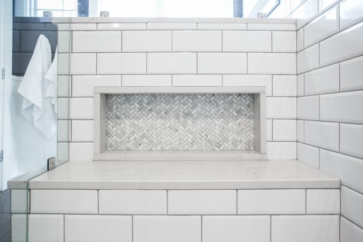 A bathroom with white tiles and a bench in the shower.