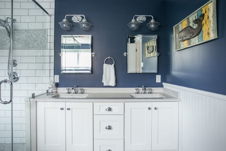 A bathroom with blue walls , white cabinets , a sink and a shower.