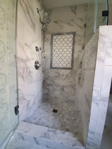 A bathroom with a walk in shower with marble tiles and a glass door.