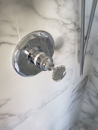A close up of a shower head and shower faucet in a bathroom.