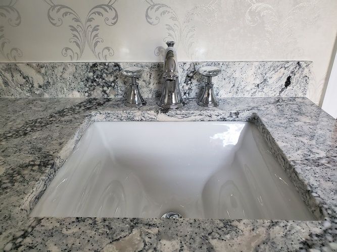 A bathroom sink is sitting on top of a granite counter top.