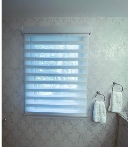 A bathroom with a window with a blind and two towels hanging on the wall.