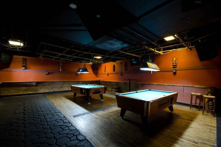 Two pool tables are sitting in a dark room.