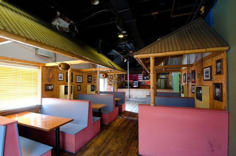 A restaurant with tables and benches and a bamboo roof