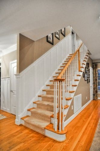 A staircase in a house with a wooden railing and a carpeted staircase.
