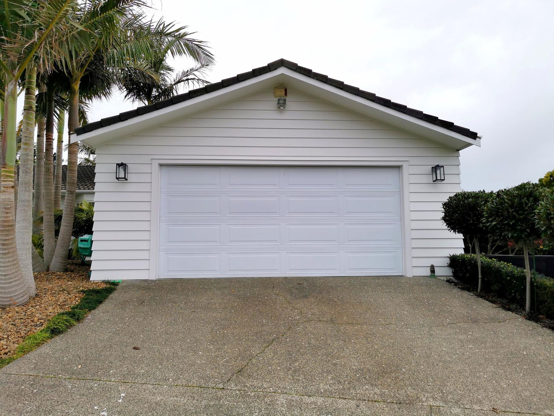 A white garage with a driveway and palm trees in the background.