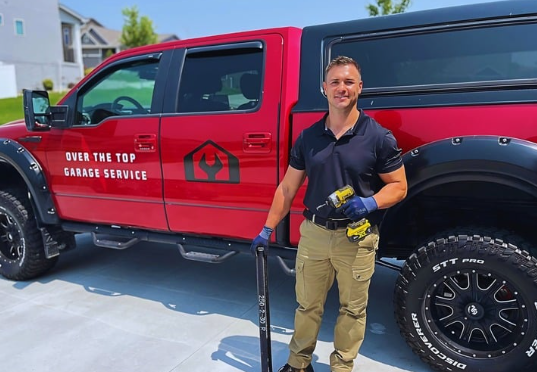 A man is standing in front of a red truck that says over the top garage service