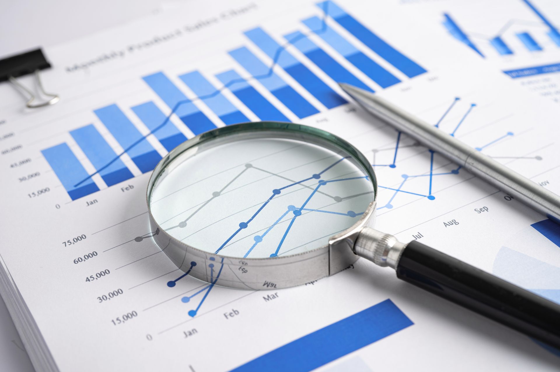 Magnifying glass on financial charts, analyzing sales data with a pen on the side.