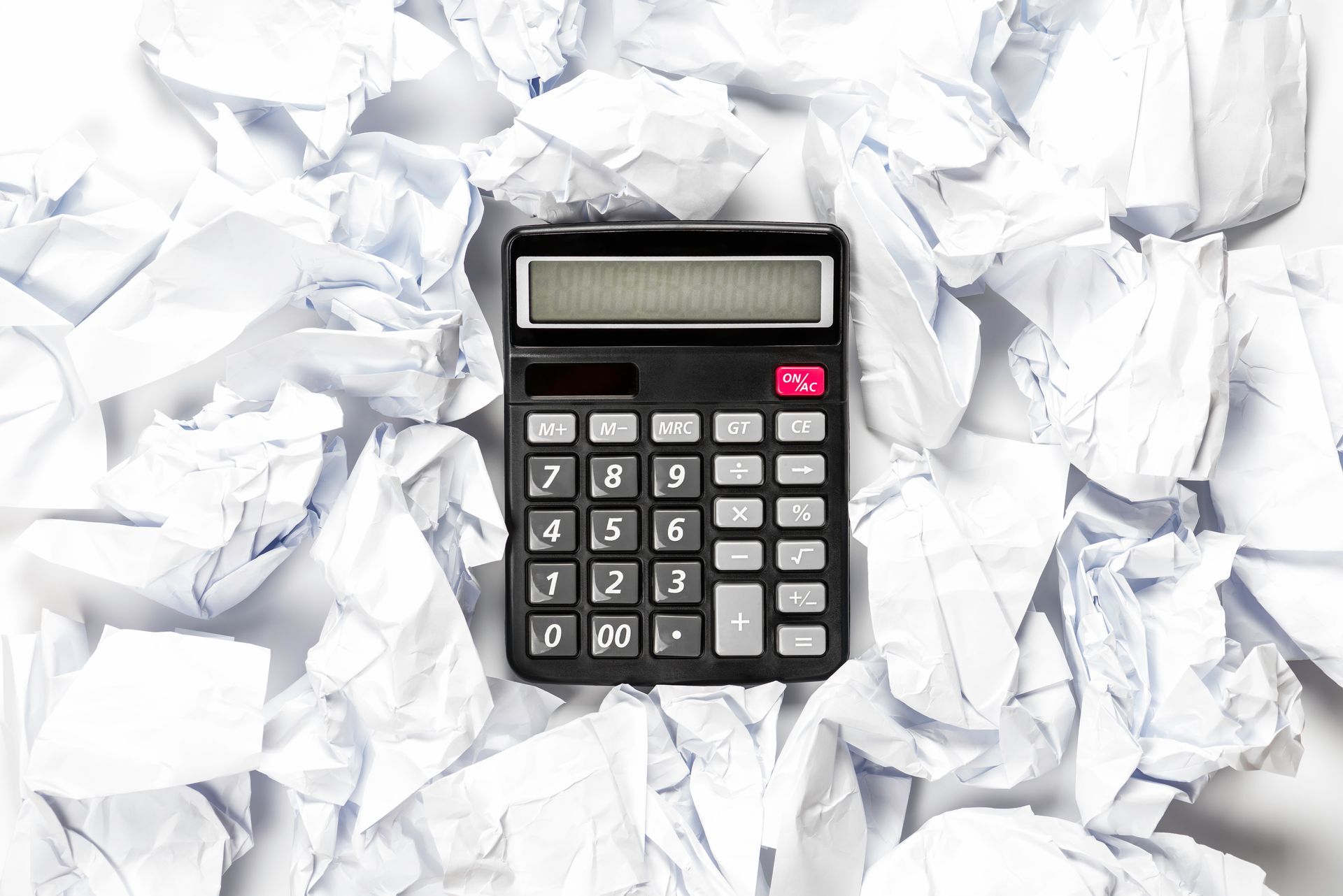 Black calculator surrounded by crumpled white paper.