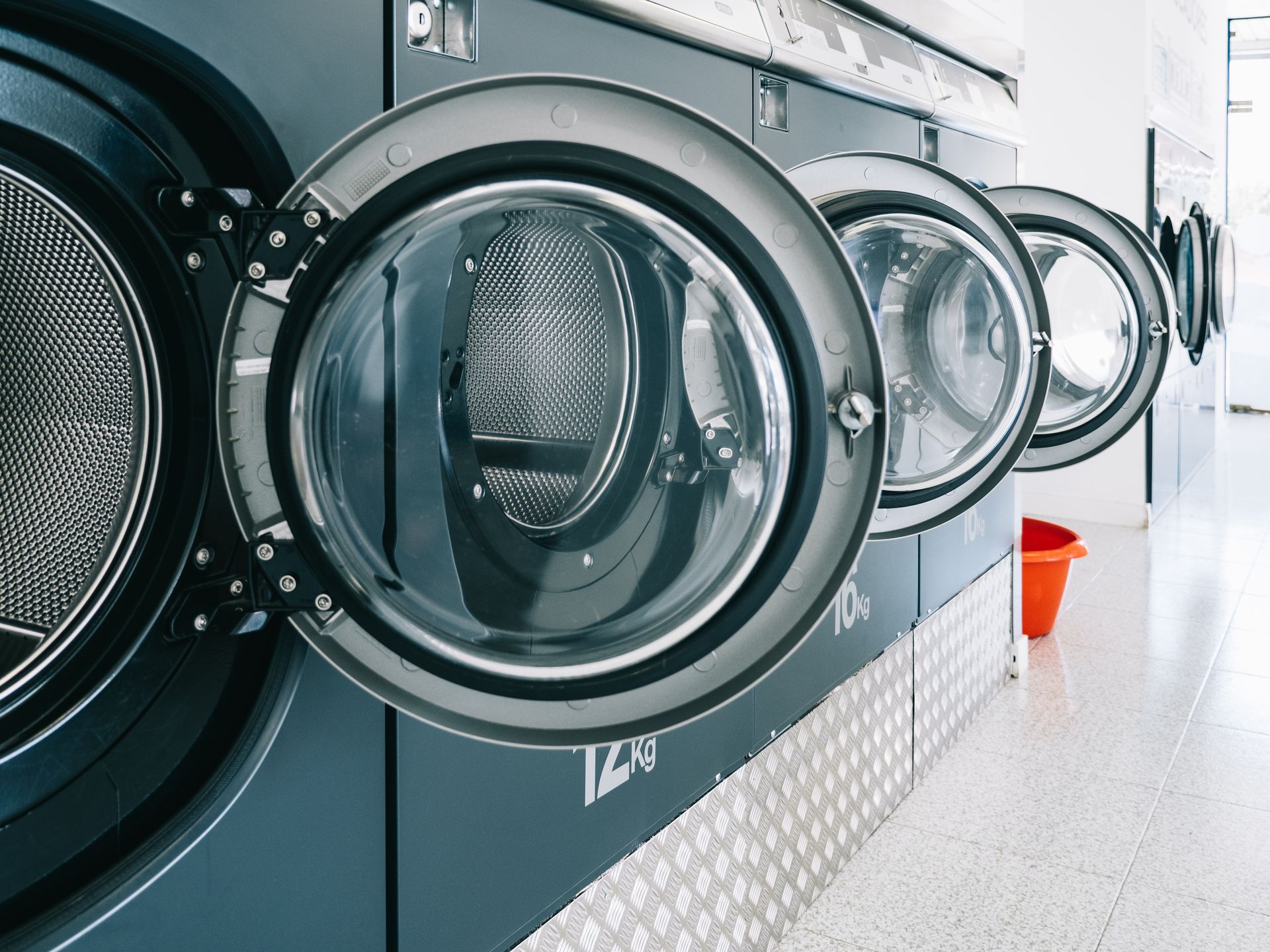 Two smiling salon staff wearing black aprons stand in a studio with brick walls and barber chairs.