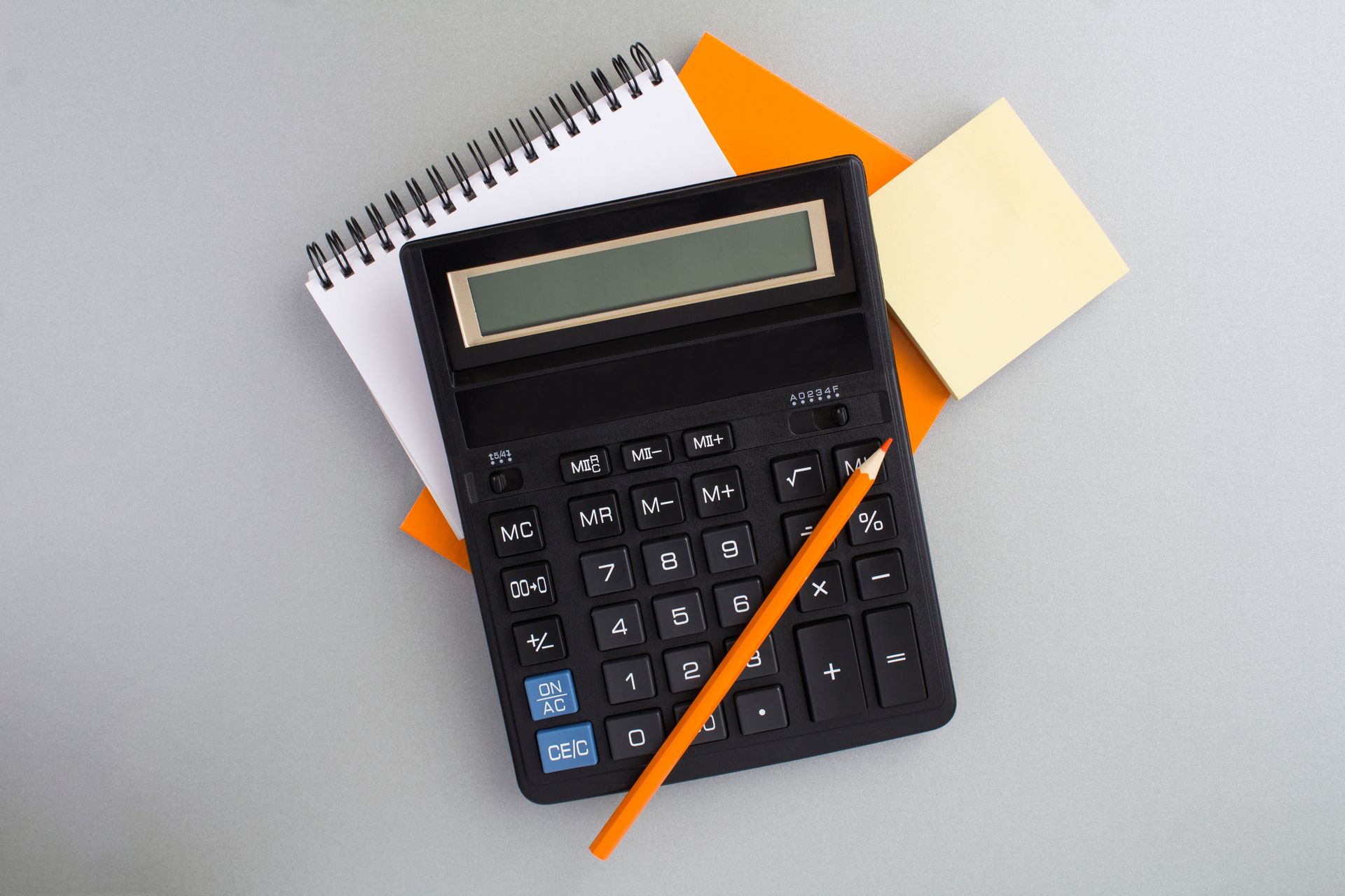 Black calculator with pencil on notebook and sticky notes.
