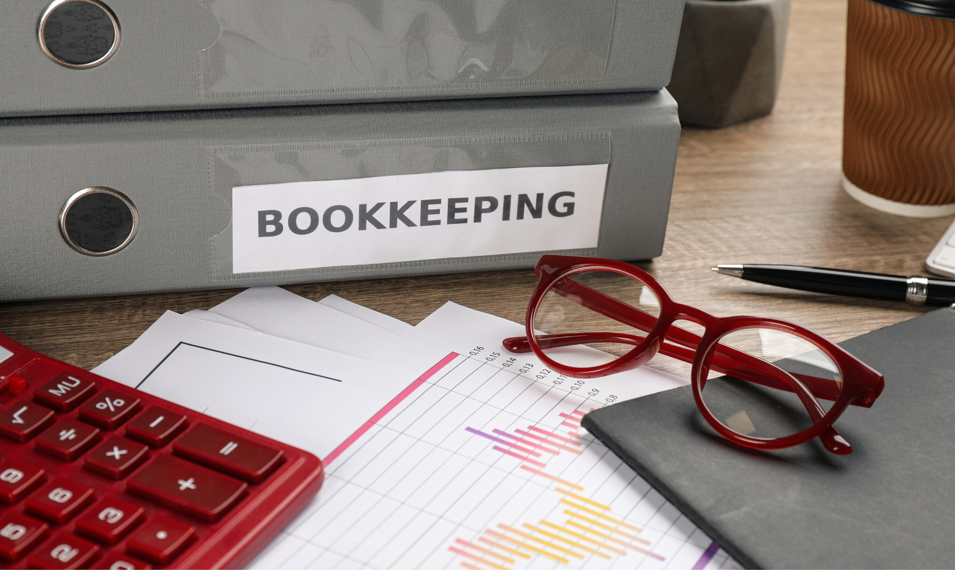 Office setting with BOOKKEEPING binder, calculator, glasses, pen, and paperwork. Office setting with BOOKKEEPING binder, calculator, glasses, pen, and paperwork.