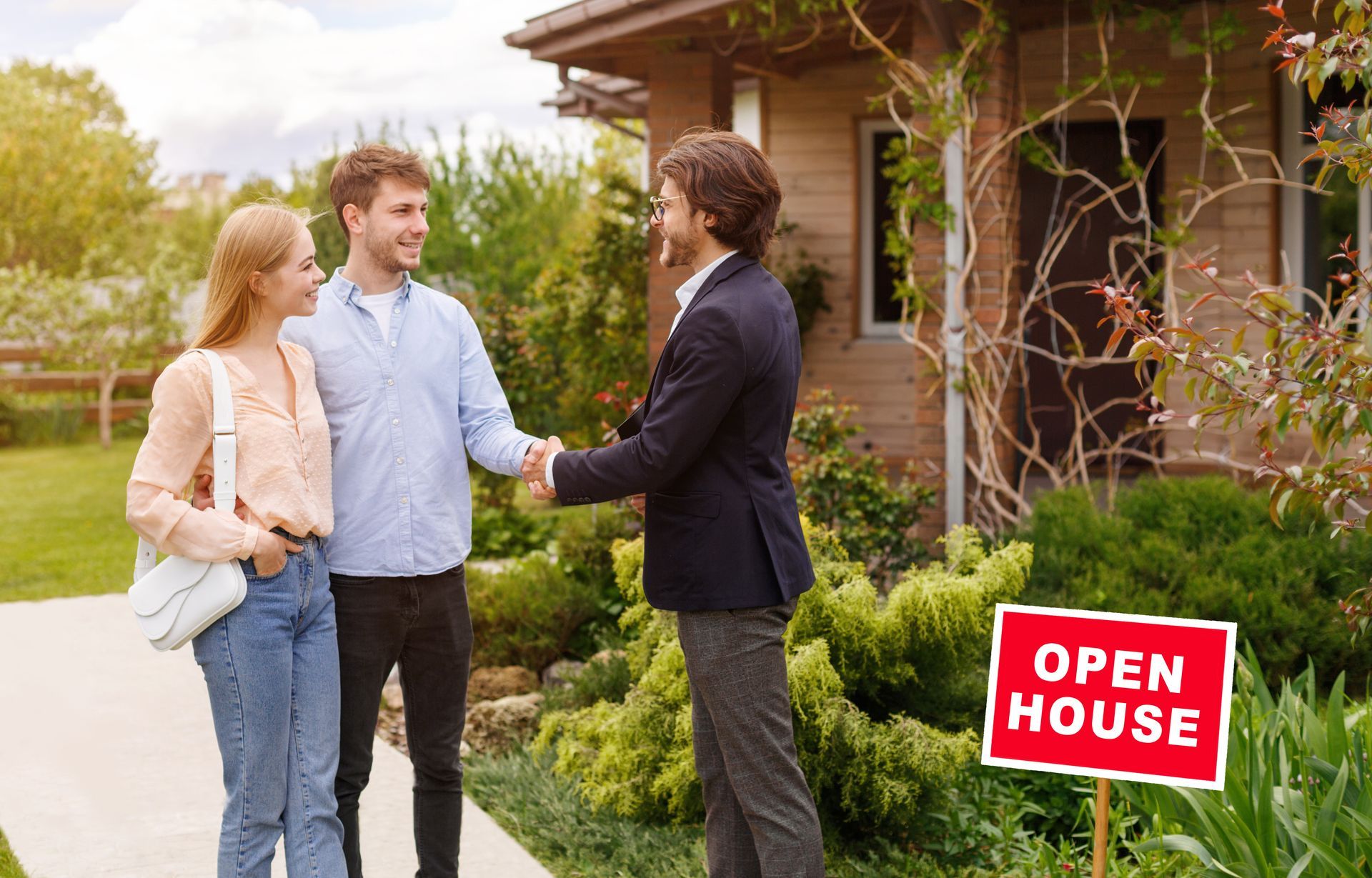 A couple shakes hands with a professional in front of a house at an open house event.