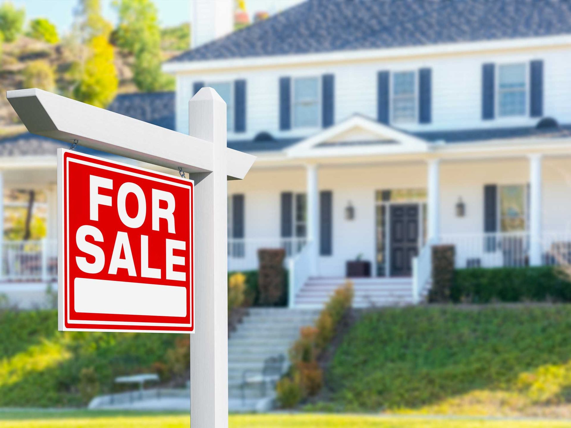 A for sale sign in front of a large white house.
