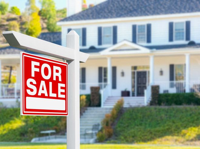 A for sale sign in front of a large white house. A for sale sign in front of a large white house.