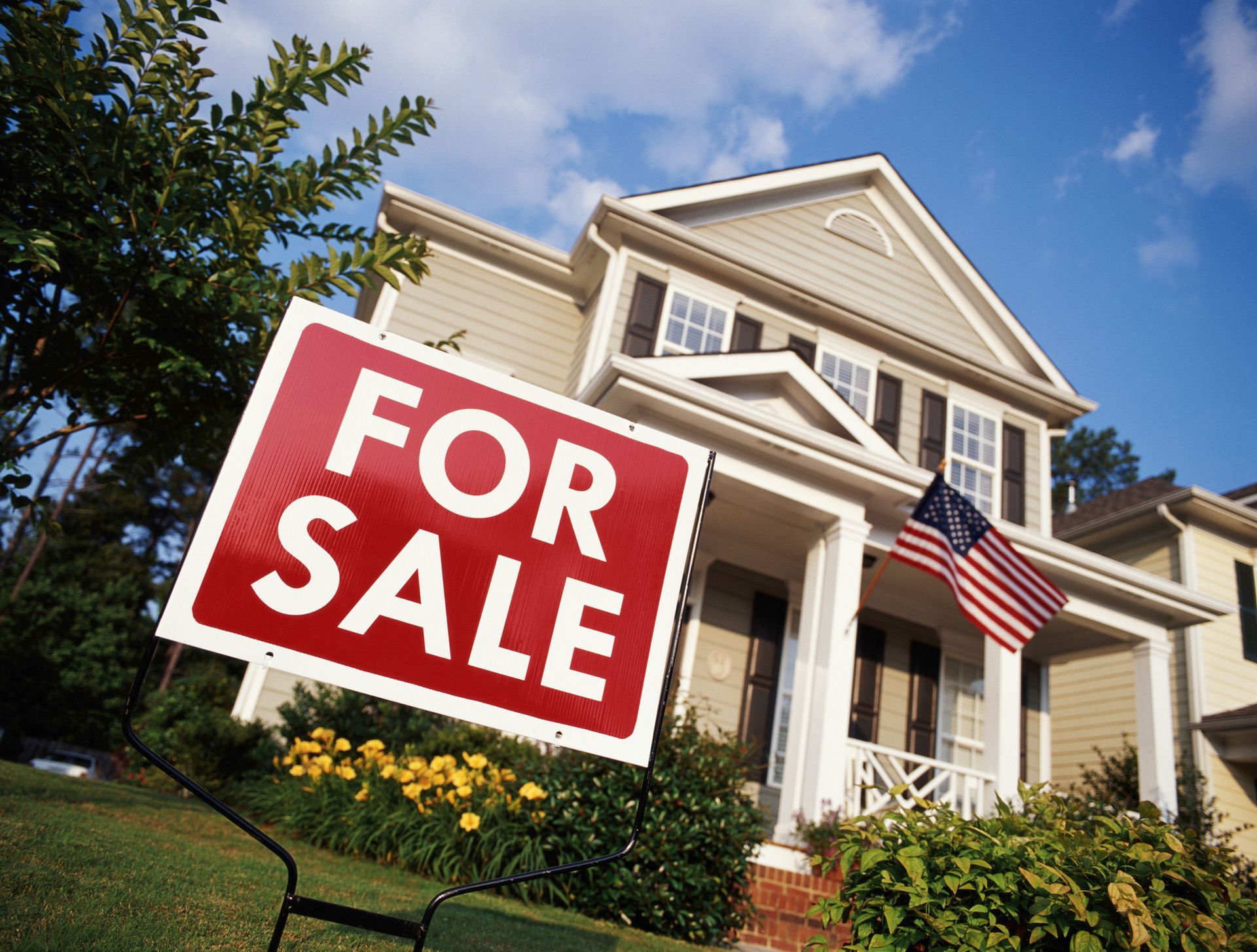 House with American flag and 'for sale' sign.
