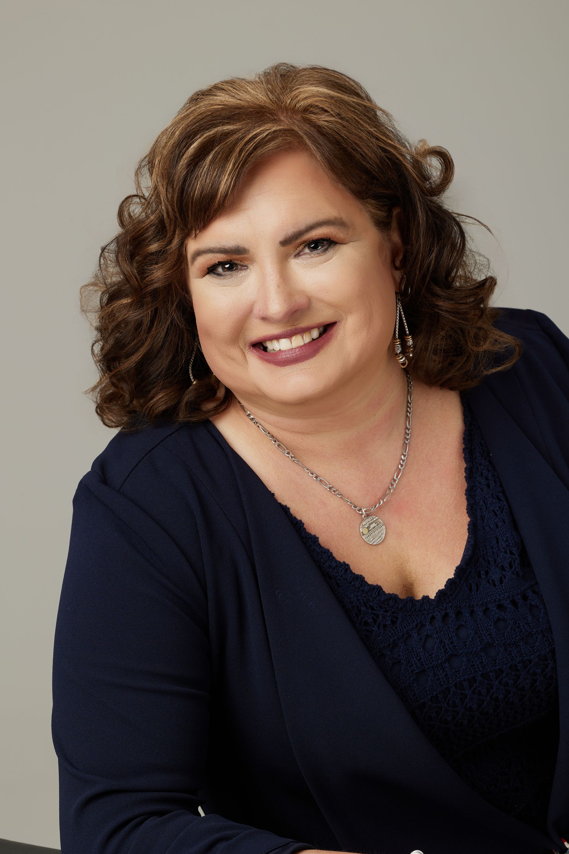 A woman wearing a blue sweater and a necklace is smiling for the camera.