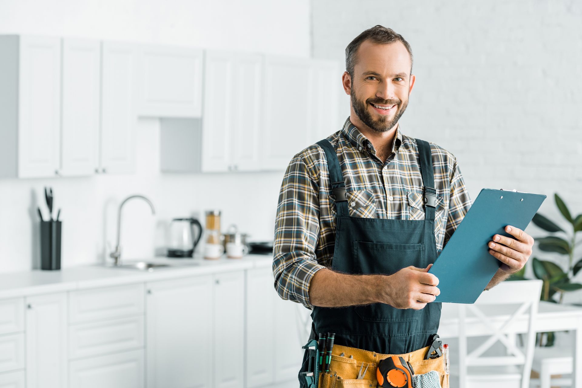 Home repair professional holding a clipboard in a bright white kitchen.