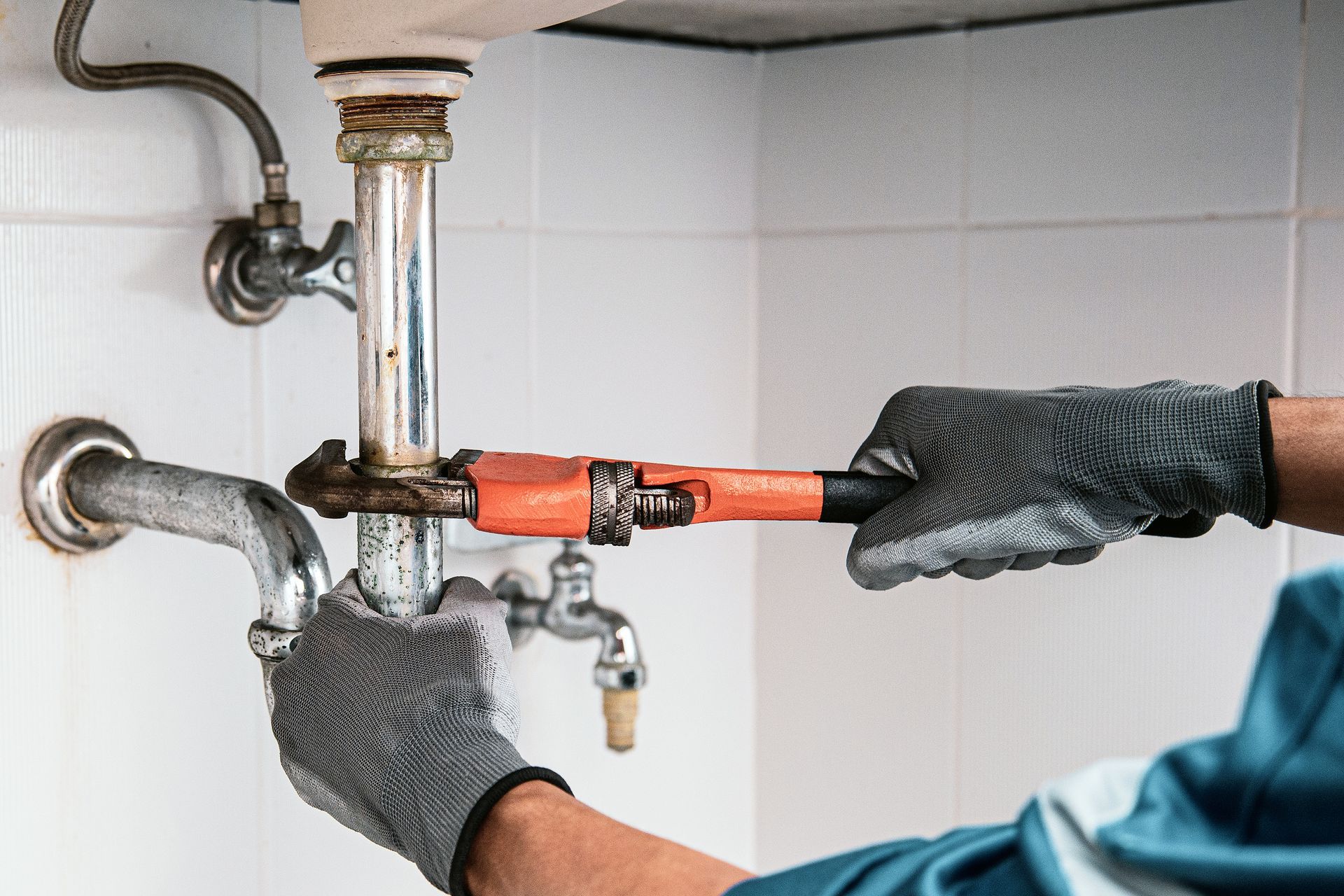 Plumber using a wrench for residential drain cleaning and fixing leaky pipes under a kitchen sink.