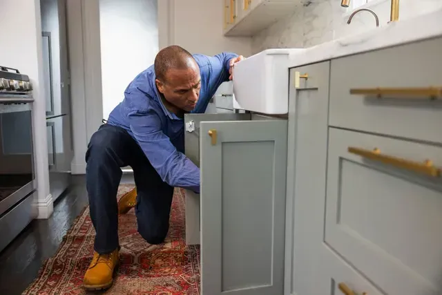 Man checking under cabinet while kneeling in kitchen.