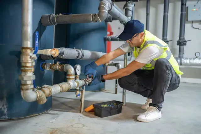 A technician in safety gear adjusts industrial pipes in a commercial plumbing environment. A technician in safety gear adjusts industrial pipes in a commercial plumbing environment.