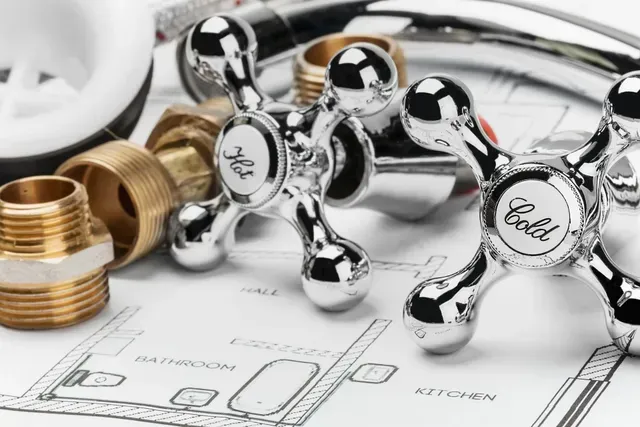 Some plumbing parts on a blueprint: hot/cold faucet handles, pipes, and connectors arranged neatly