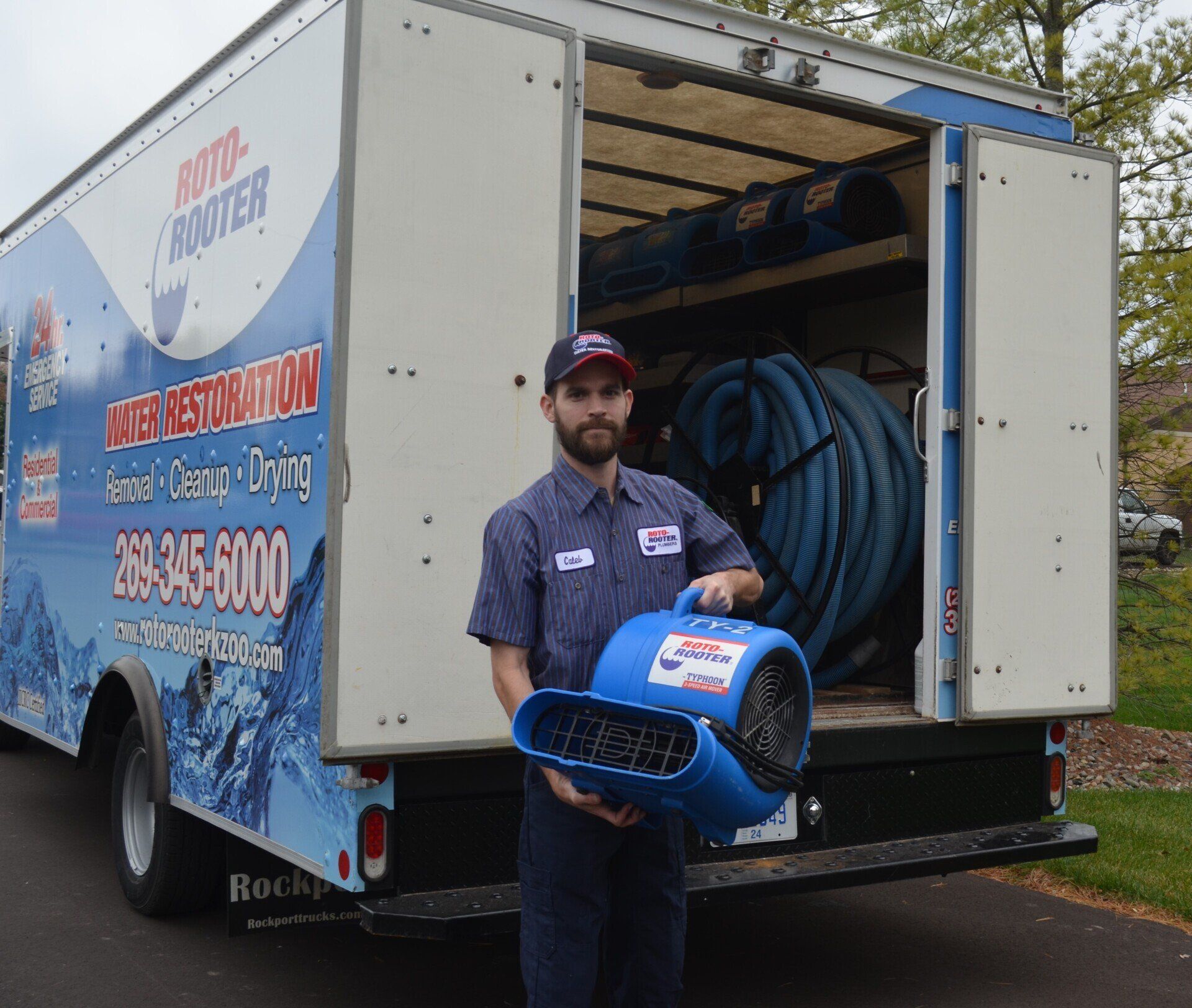 A man is holding a blue fan in front of a carpet restoration truck