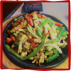 a black plate topped with chicken and vegetables on a wooden table .
